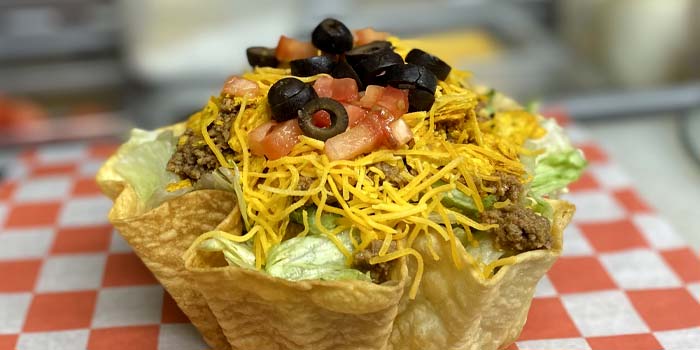 Taco Salad topped with black olives, diced tomatoes, cheddar cheese, meta and lettuce wrapped in a taco shell bowl at Butch's Pizza The Best Pizzeria in Kimberly WI and the Fox Valley